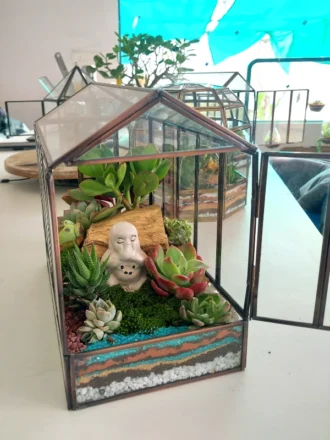 “Garden Glass House Terrarium by Wild Roots – a handcrafted glass house-shaped terrarium featuring lush green indoor plants, designed as an elegant décor piece and eco-friendly gift for home, office, or special occasions. Perfect for adding freshness, charm, and natural beauty to interiors with minimal maintenance.”